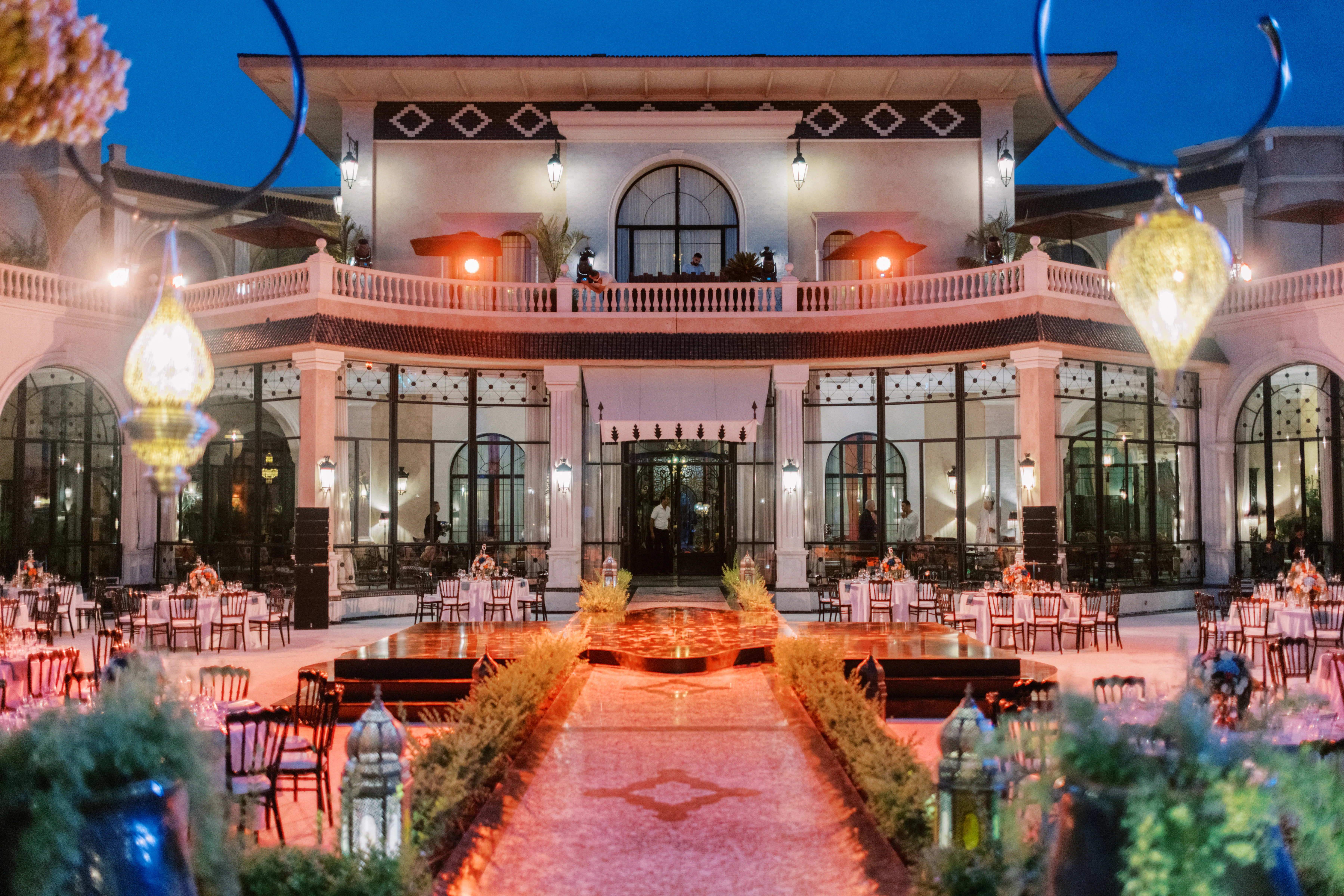 Refined two-story building with a platform in front of it. On the sides of the platform there are circular tables with chairs for guests.